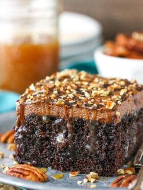 A square serving of Chocolate Turtle Poke Cake next to a silver fork on a gray plate