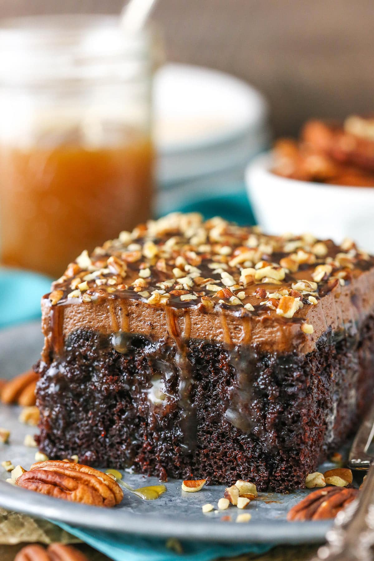 A square serving of Chocolate Turtle Poke Cake next to a silver fork on a gray plate