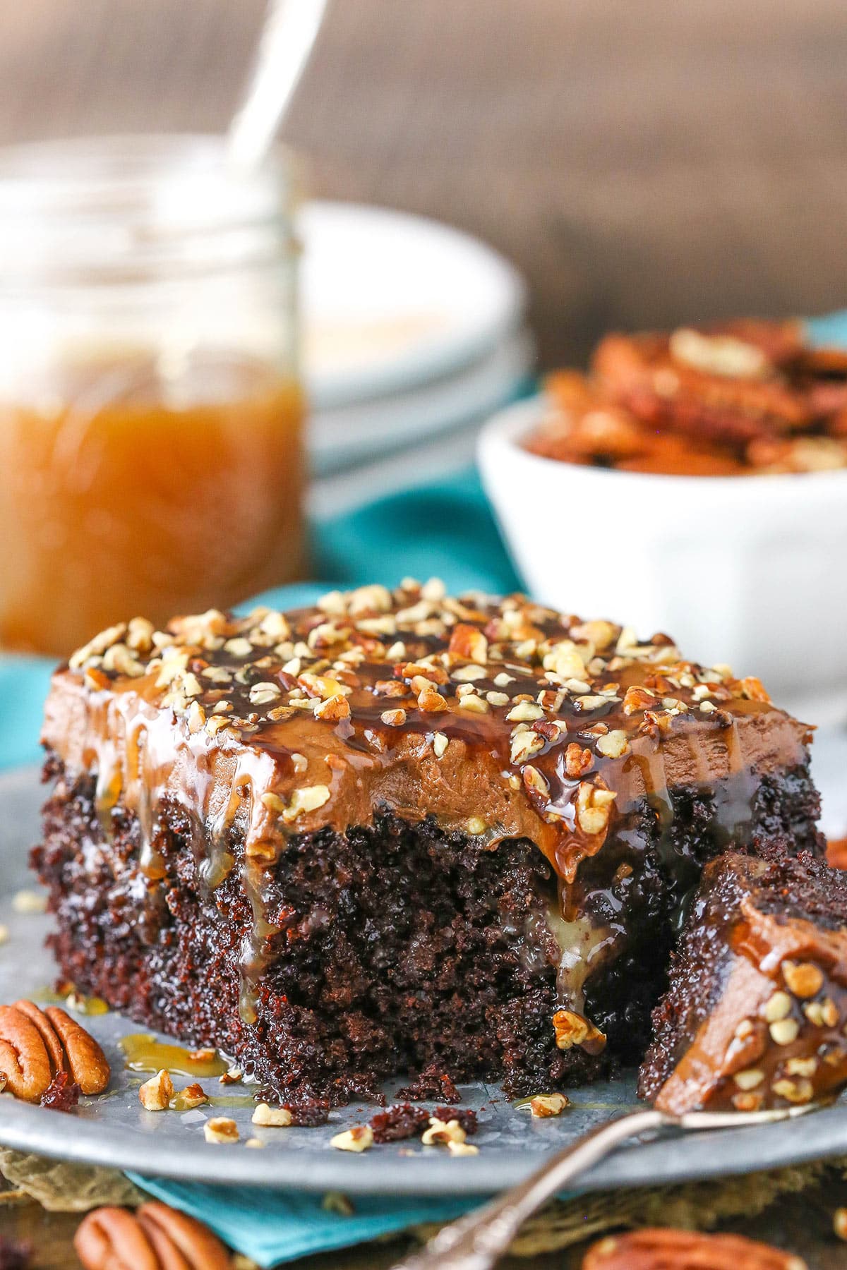 A square serving of Chocolate Turtle Poke Cake with a bite removed next to a silver fork on a gray plate