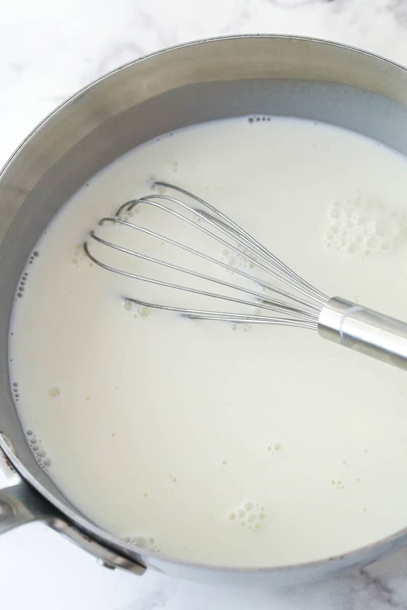 Whisking milk into a mixture of sugar, flour, and salt in a saucepan.