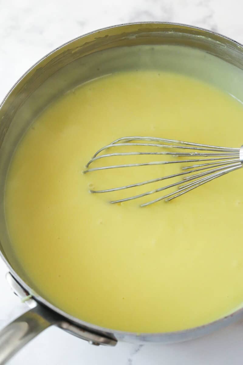 Whisking tempered egg yolks into a pudding base and letting the mixture thicken.