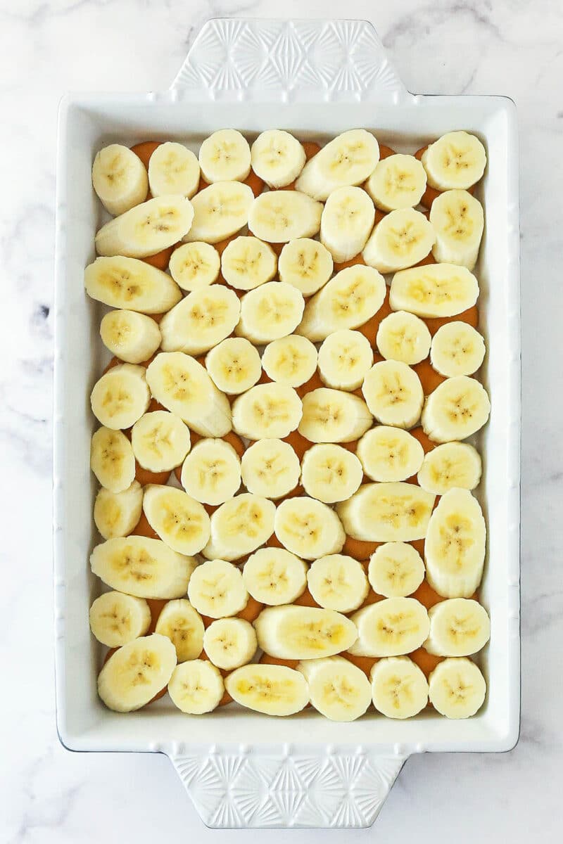 Layering banana slices over a layer of vanilla wafters in a baking dish.
