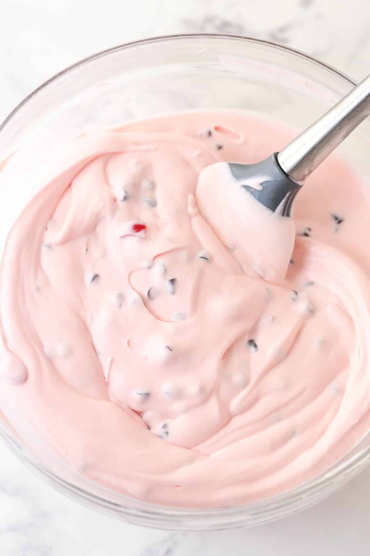 Folding mini chocolate chips and maraschino cherries into cherry ice cream.