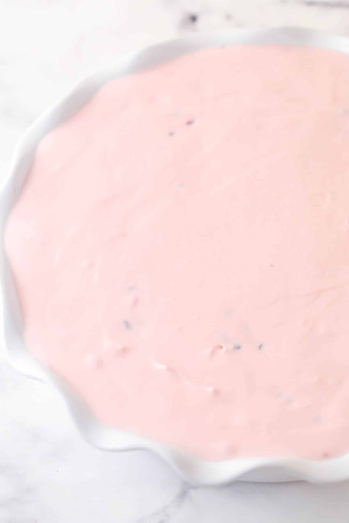 Cherry chocolate chip ice cream pie is made of Oreo crust, cherry ice cream with mini chocolate chips and cherry chunks, and whipped cream. Adding cherry chocolate ice cream to a pie dish.