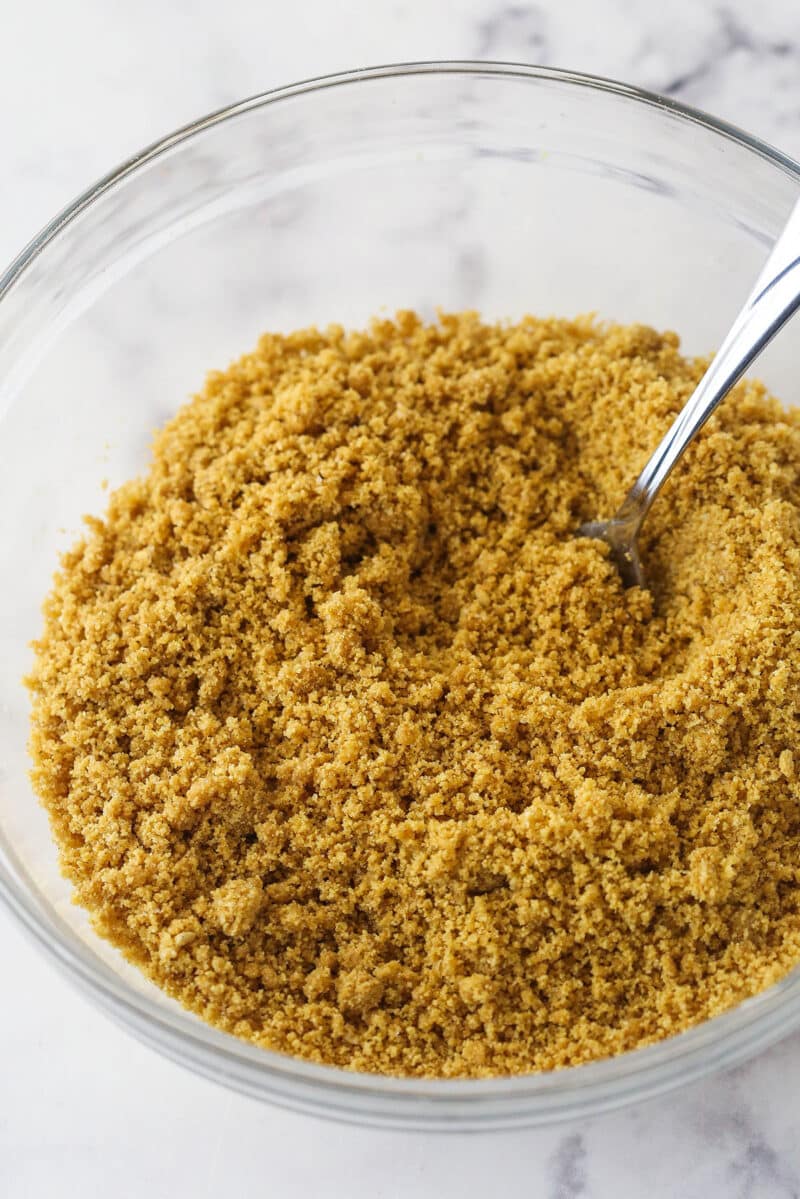 This lemon tart is made up of graham cracker crust, a sweet and tangy, creamy lemon filling, and a fluffy whipped cream topping. Mixing together graham cracker crumbs, butter, and sugar to make graham cracker crust.