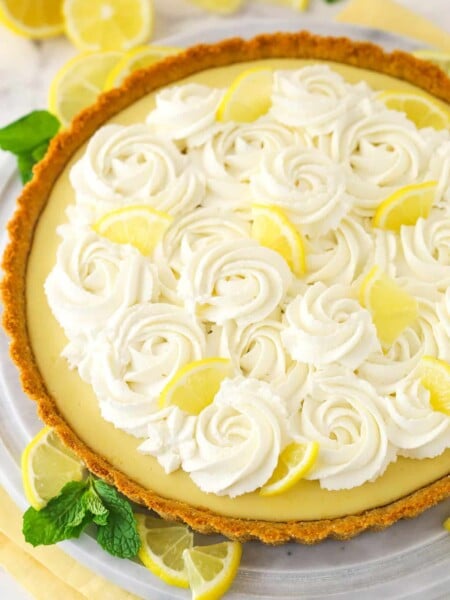 A whole lemon tart surrounded by lemon slices.