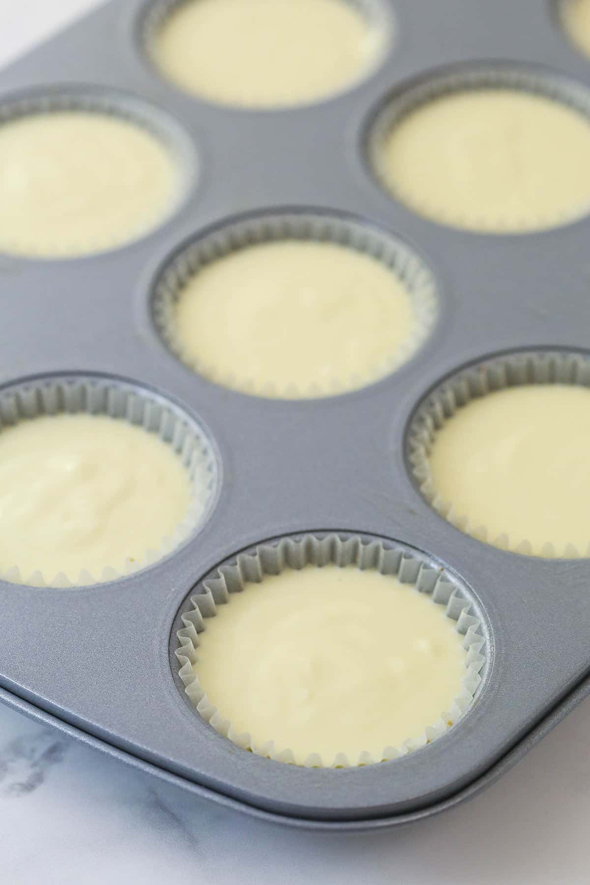 Mini strawberry cheesecakes are made of graham cracker crusts, thick, creamy vanilla cheesecake filling, and sweet strawberry sauce. Vanilla cheesecake filling in cupcake liners in a cupcake pan.