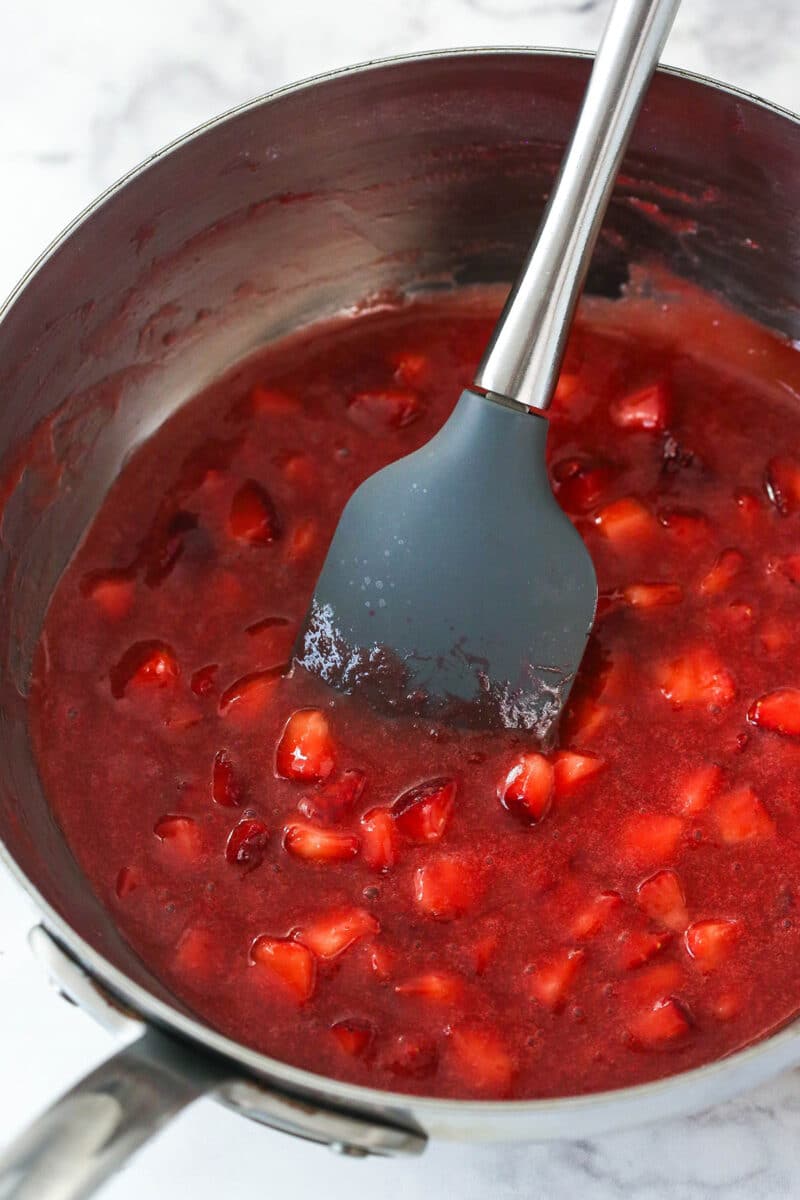 Mini strawberry cheesecakes are made of graham cracker crusts, thick, creamy vanilla cheesecake filling, and sweet strawberry sauce. Stirring strawberry topping for mini strawberry cheesecakes.