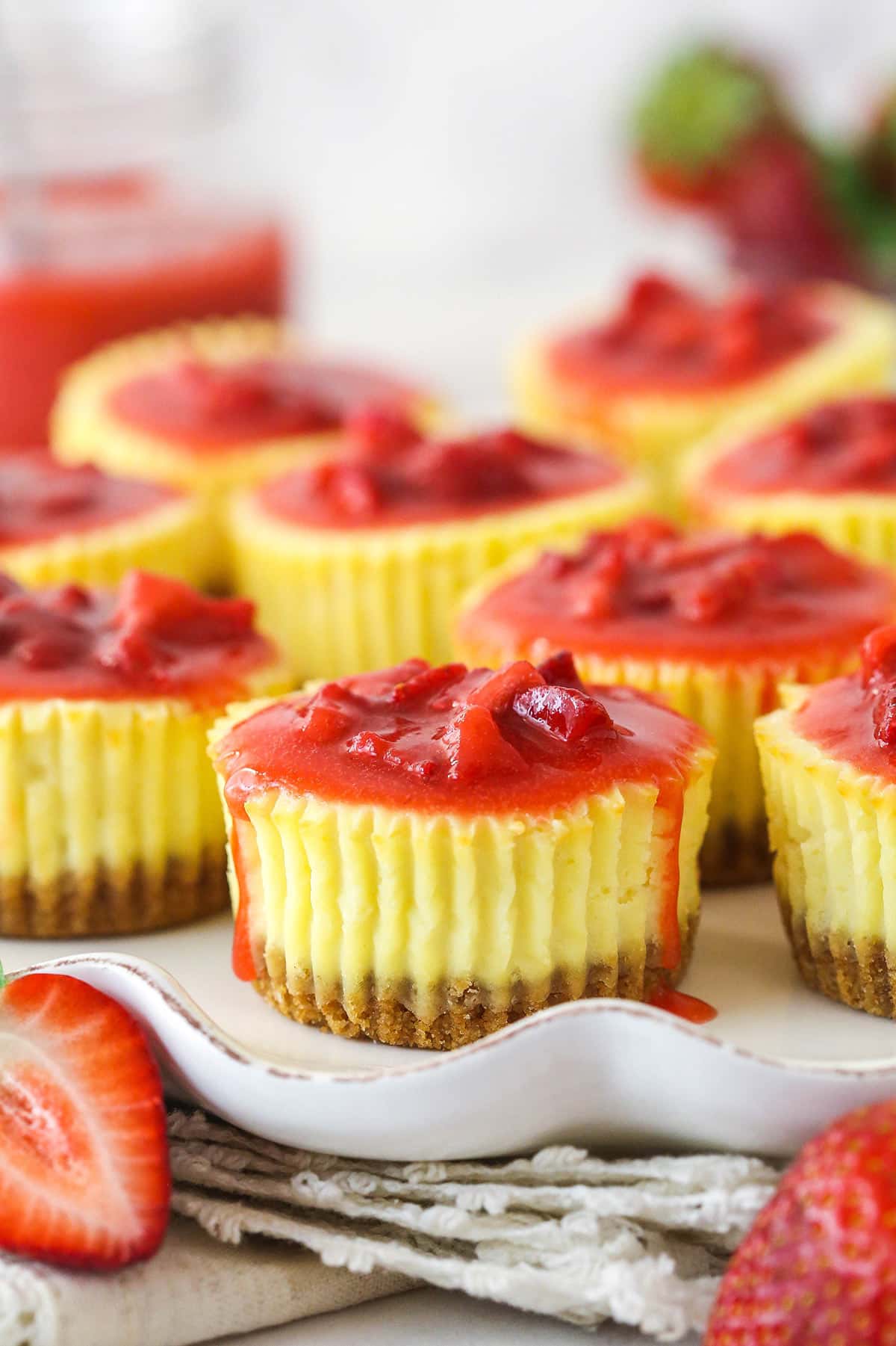 Mini strawberry cheesecakes are made of graham cracker crusts, thick, creamy vanilla cheesecake filling, and sweet strawberry sauce. Mini strawberry cheesecakes on a serving platter.