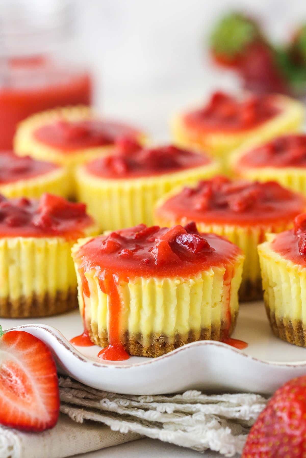 Mini strawberry cheesecakes are made of graham cracker crusts, thick, creamy vanilla cheesecake filling, and sweet strawberry sauce. Mini strawberry cheesecakes with sauce dripping down the sides.