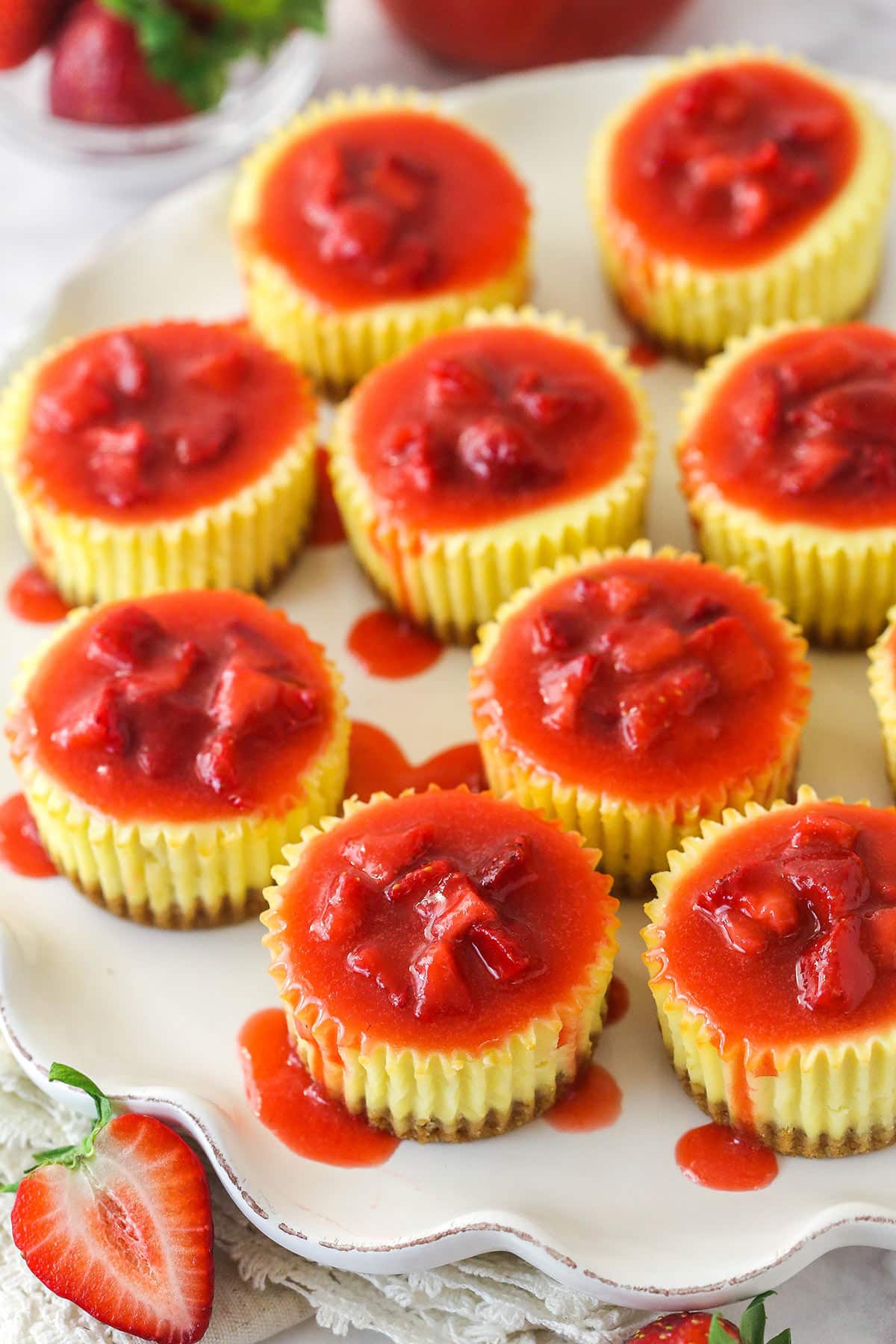 Mini strawberry cheesecakes are made of graham cracker crusts, thick, creamy vanilla cheesecake filling, and sweet strawberry sauce. Overhead image of mini strawberry cheesecakes on a serving platter.