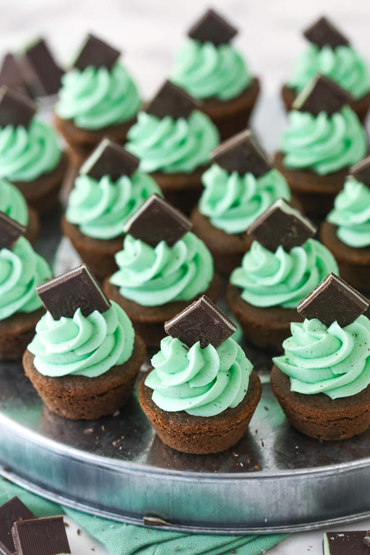mint chocolate cookie cups frosted with mint buttercream and topped with Andes mint on a silver platter and green napkin