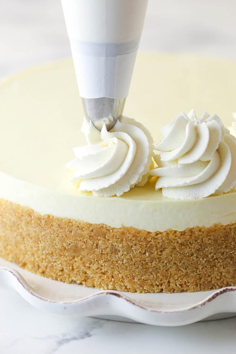 Piping whipped cream onto no bake lemon cheesecake.