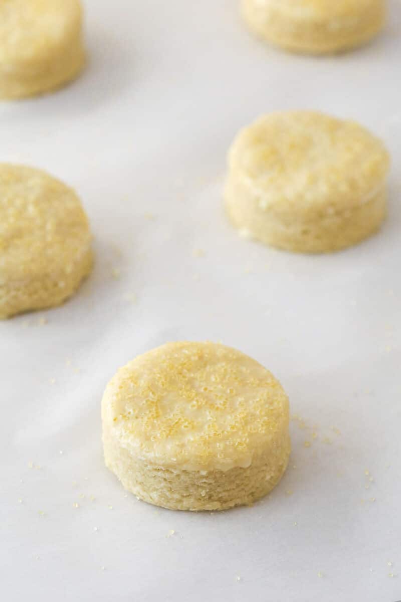 This strawberry shortcake recipe turns out cute, individual desserts made of flaky biscuits stuffed with juicy strawberries and whipped cream. Unbaked shortcake biscuits sprinkled with sugar on a sheet of parchment paper.