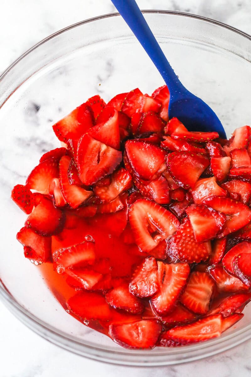 This strawberry shortcake recipe turns out cute, individual desserts made of flaky biscuits stuffed with juicy strawberries and whipped cream. Strawberries coated in sugar in a bowl, releasing their juices.