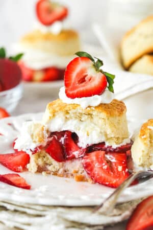 Strawberry shortcake on a plate with a couple of bites taken out of it.