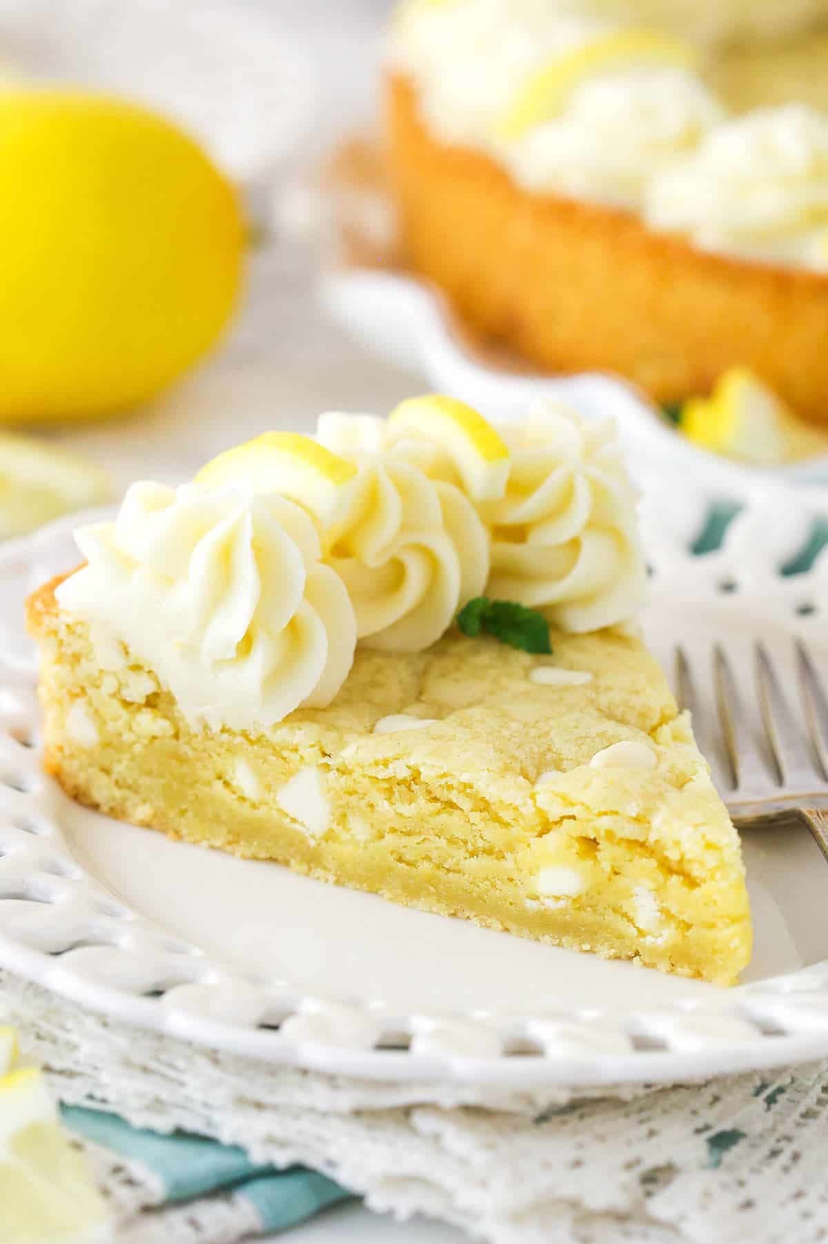 This lemon cookie cake is perfect for summer! Topped with lemon cream cheese frosting, it's soft and chewy with a lovely light lemon flavor. A slice of lemon cookie cake on a plate.