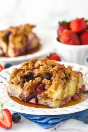 A slice of berry French toast casserole served on a plate with maple syrup.