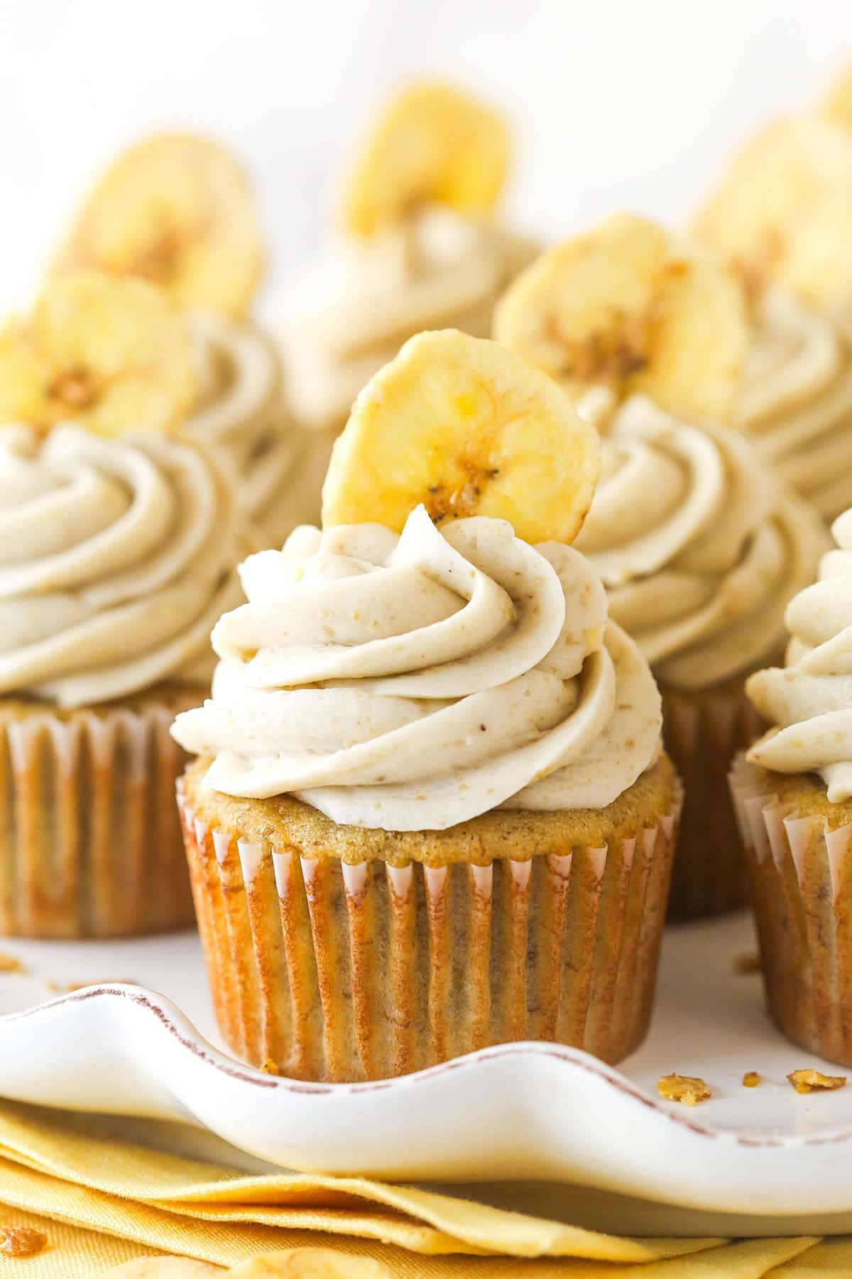 These banana cream pie cupcakes are too good! Moist, fluffy banana cupcakes are filled with vanilla custard and topped with banana frosting. Closeup image of banana cream pie cupcakes on a serving platter.