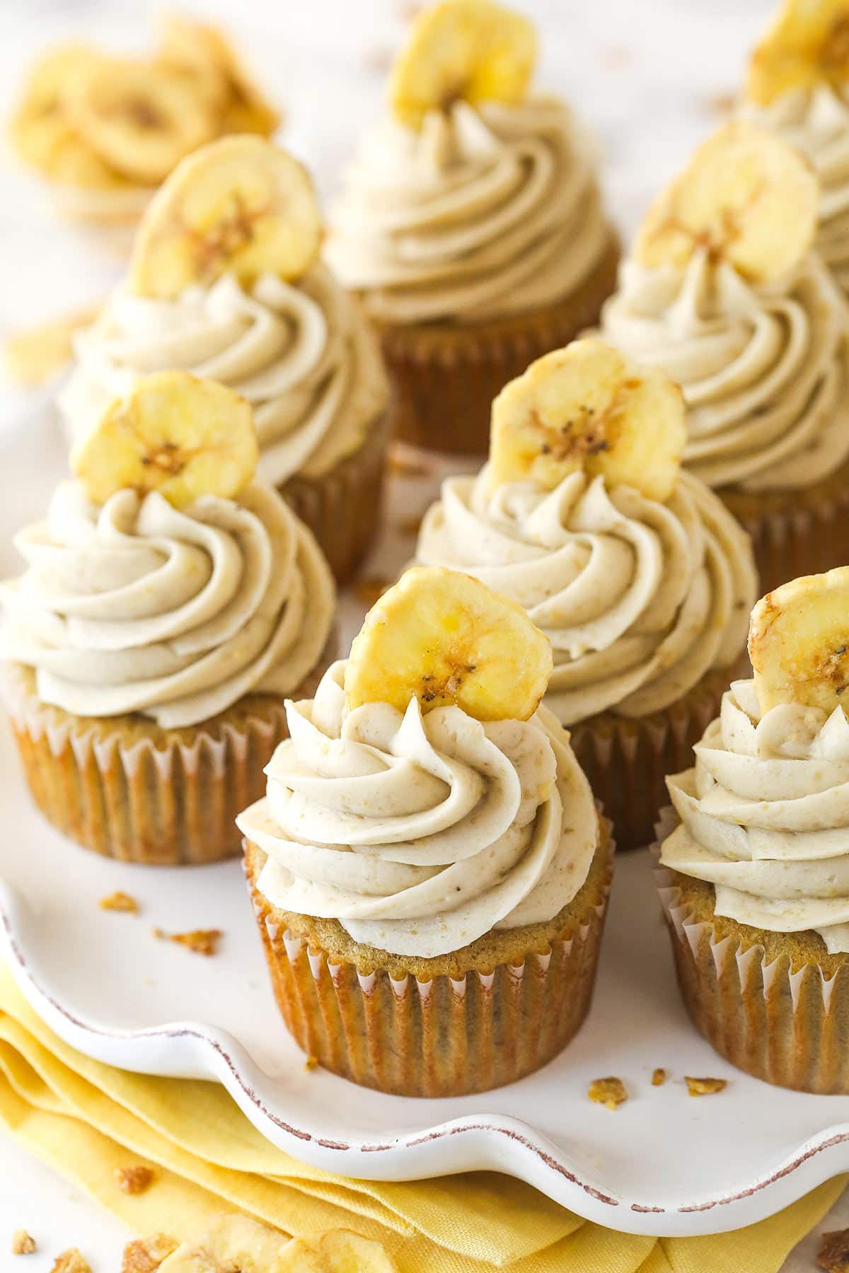 These banana cream pie cupcakes are too good! Moist, fluffy banana cupcakes are filled with vanilla custard and topped with banana frosting. Overhead image of banana cream pie cupcakes on a serving platter.