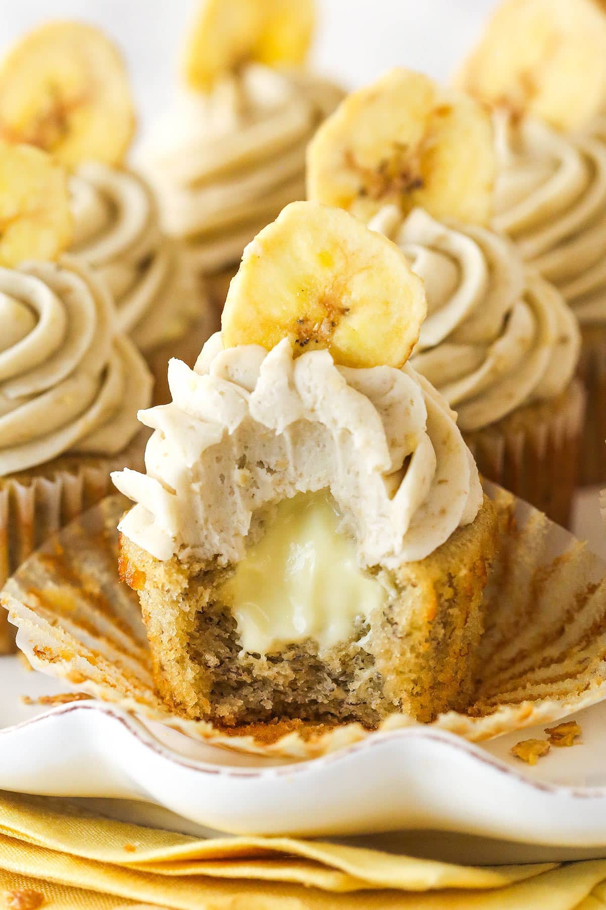 These banana cream pie cupcakes are too good! Moist, fluffy banana cupcakes are filled with vanilla custard and topped with banana frosting. A banana cream pie cupcake with a bite taken out of it.