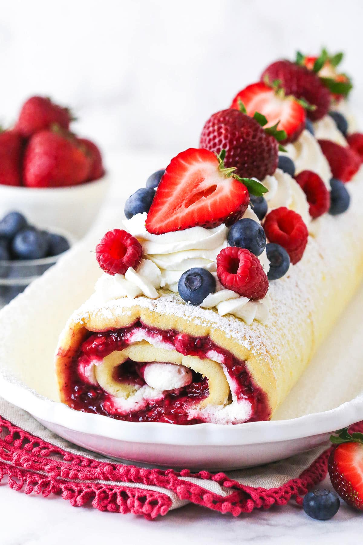 decorated Berry Vanilla Cake Roll on a white platter with berries in the background