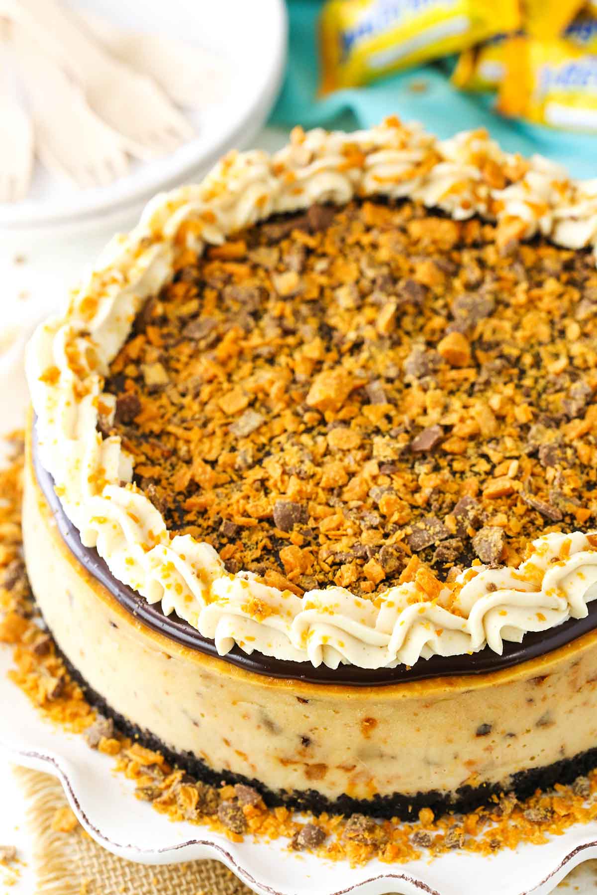 Side view of a full Butterfinger Cheesecake on a white cake stand