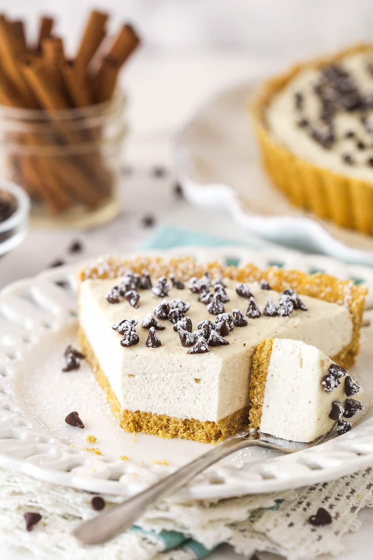 With a hint of cinnamon and some mini chocolate chips, this cannoli tart has all the great flavors of a cannoli wrapped into one simple tart. A fork taking a bite out of a slice of cannoli tart on a plate.