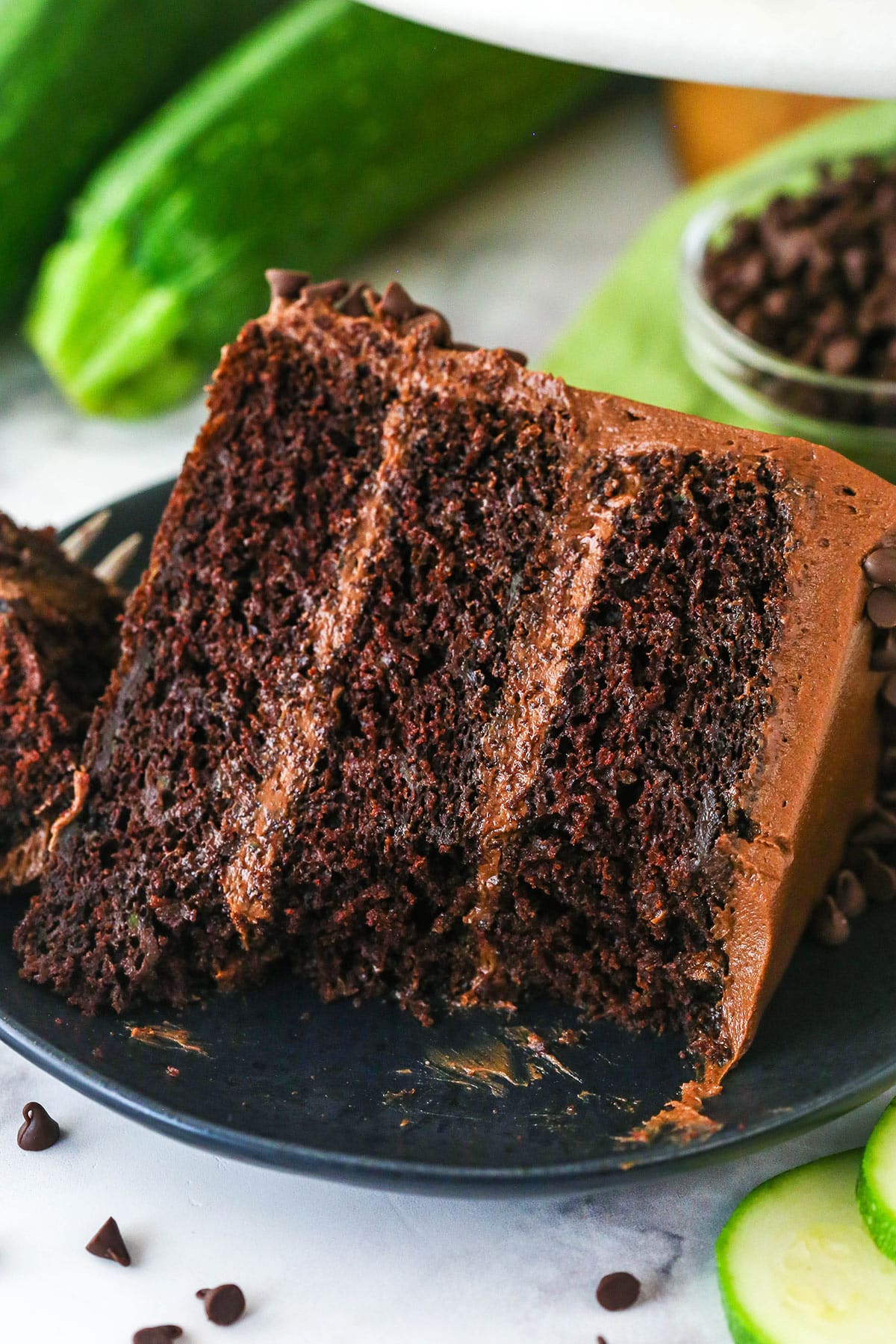This Chocolate Zucchini Cake is so dreamy! 3 moist, zucchini-loaded chocolate cake layers are filled and frosted with chocolate buttercream. A slice of chocolate zucchini cake on a plate with a bite taken out of it.