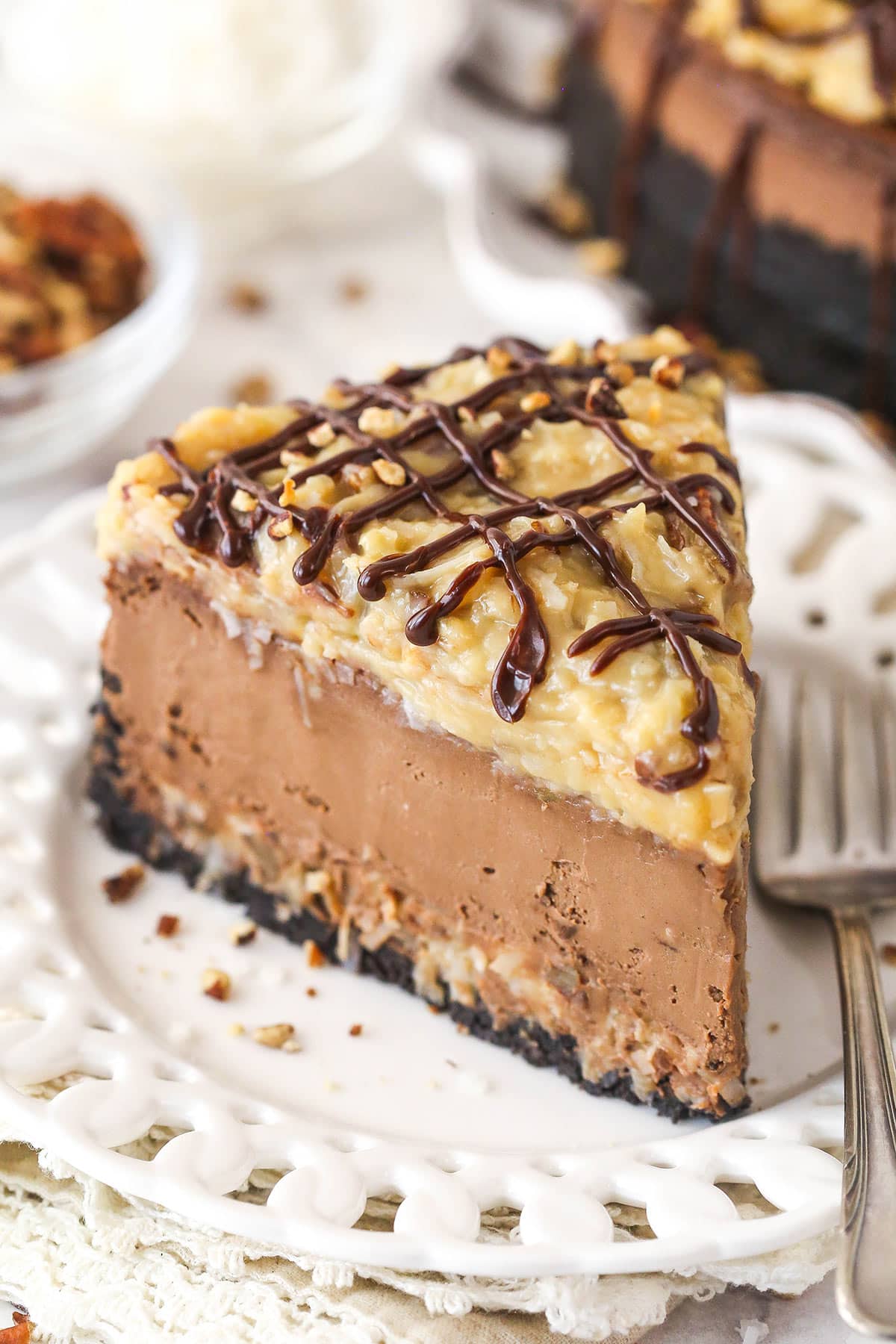 This German Chocolate Cheesecake with layers of creamy German chocolate cheesecake and gooey coconut pecan topping is out of this world! A slice of German chocolate cheesecake on a plate with a fork.