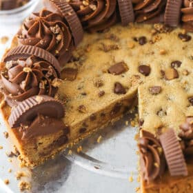Reese's peanut butter cookie cake on a serving plate with a slice taken out of it.