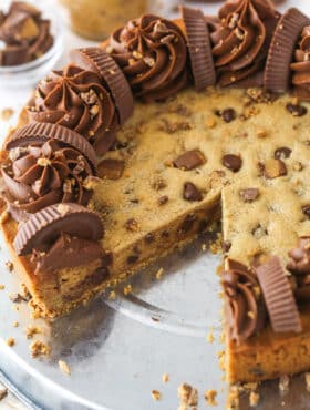Reese's peanut butter cookie cake on a serving plate with a slice taken out of it.