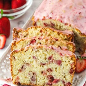 A loaf of strawberry bread with 3 slices leaning up against it.