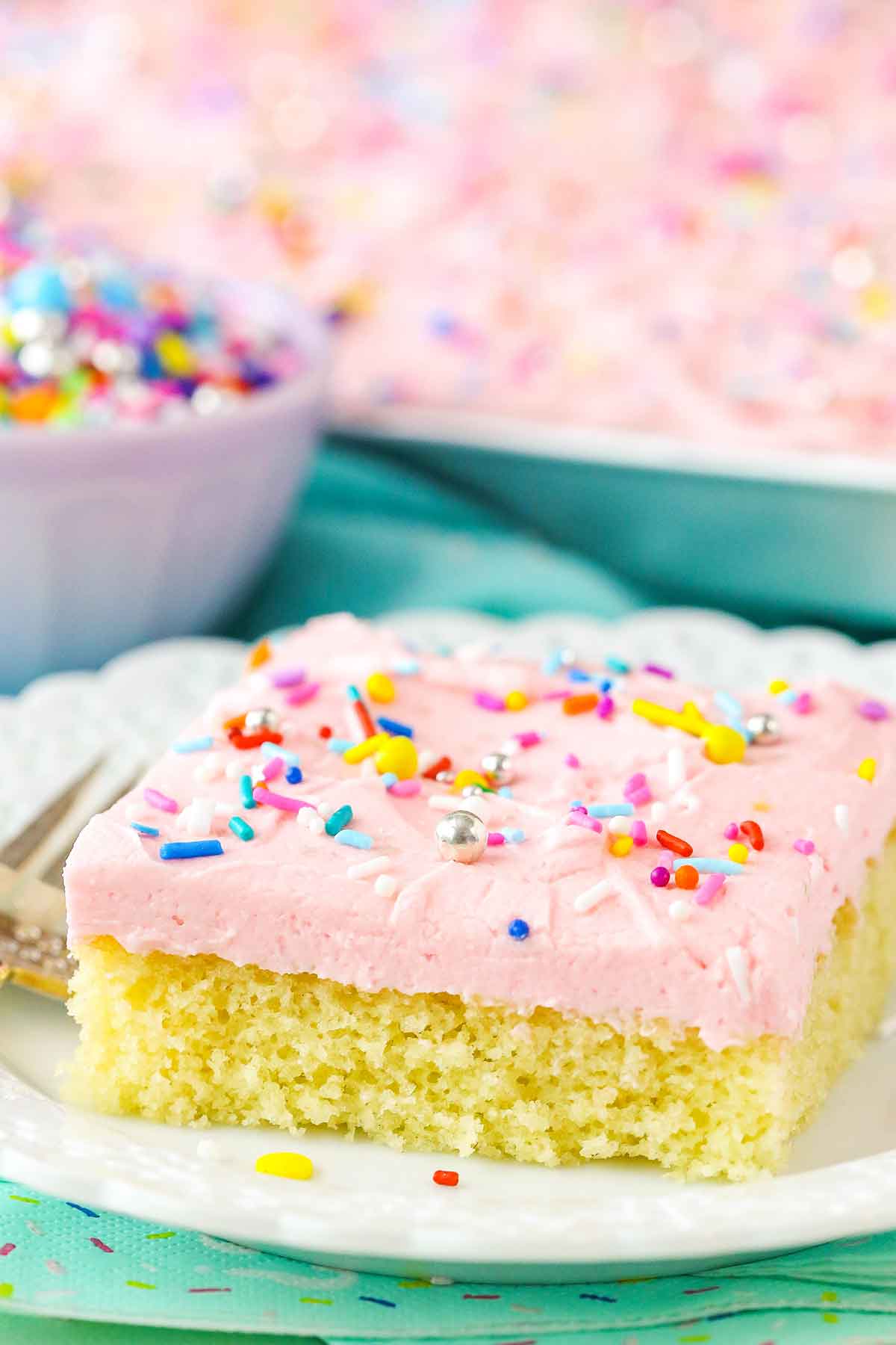A square slice of Vanilla Sheet Cake next to a fork on a white plate