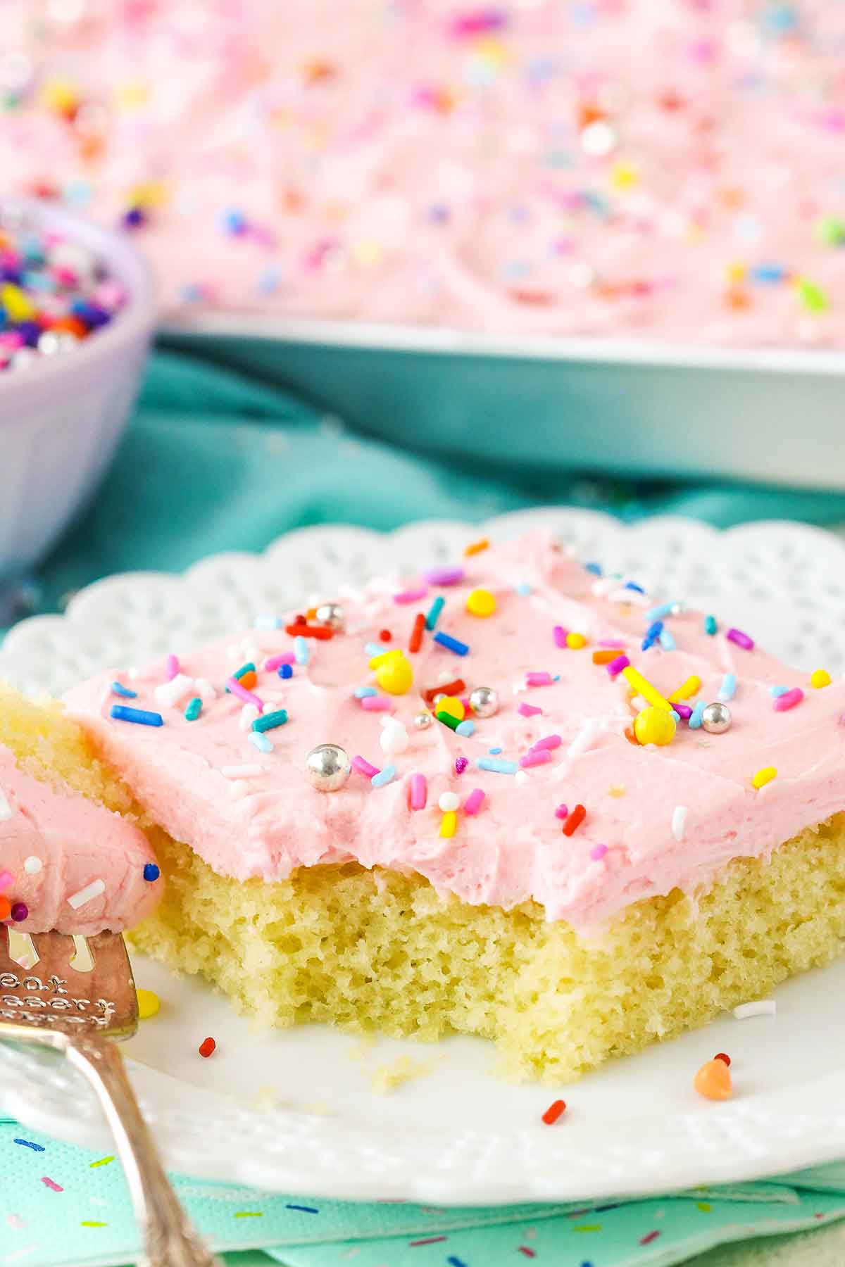 A square slice of Vanilla Sheet Cake with a bite removed next to a fork on a white plate