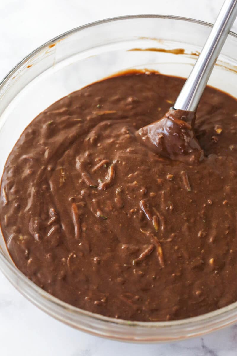 This Chocolate Zucchini Cake is so dreamy! 3 moist, zucchini-loaded chocolate cake layers are filled and frosted with chocolate buttercream. Folding shredded zucchini into chocolate cake batter.