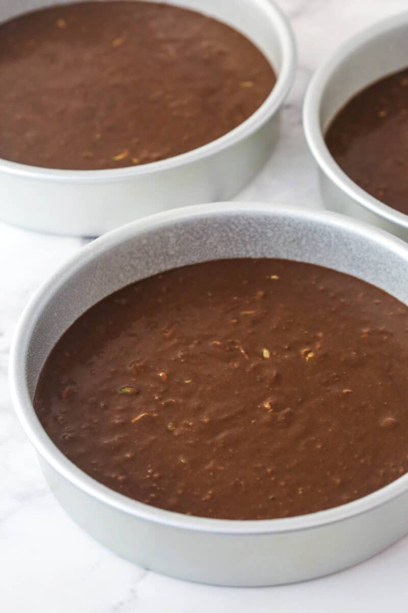 This Chocolate Zucchini Cake is so dreamy! 3 moist, zucchini-loaded chocolate cake layers are filled and frosted with chocolate buttercream. Chocolate zucchini cake batter divided between 3 cake pans.