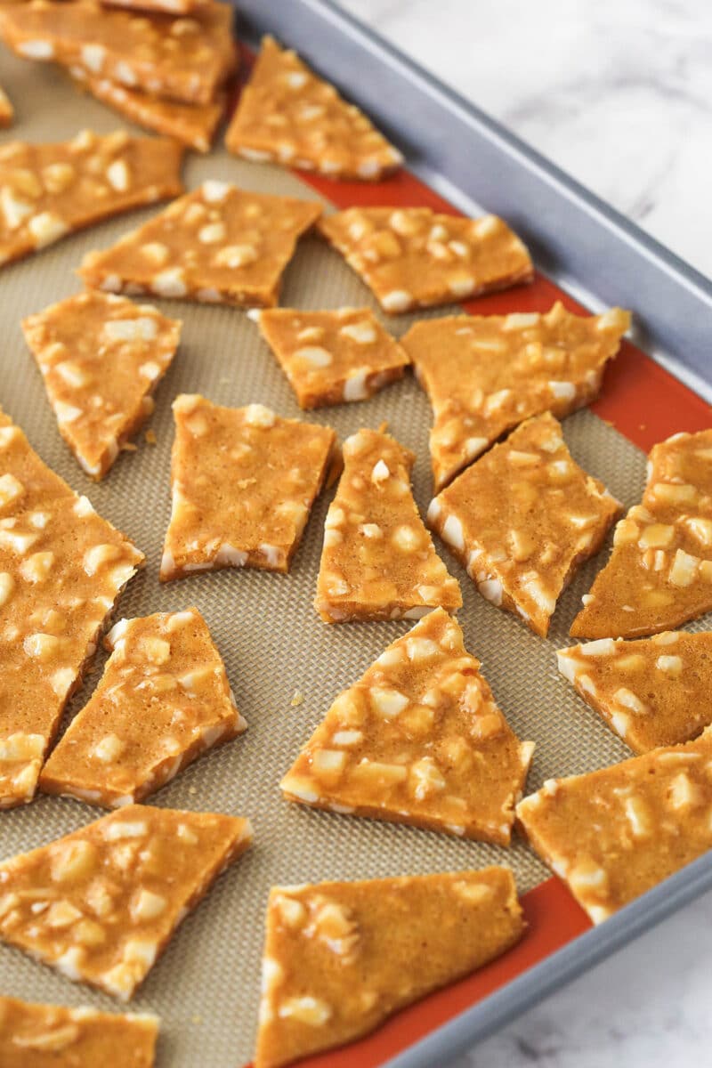 Pieces of Macadamia Brittle on a silicone mat on a baking sheet.