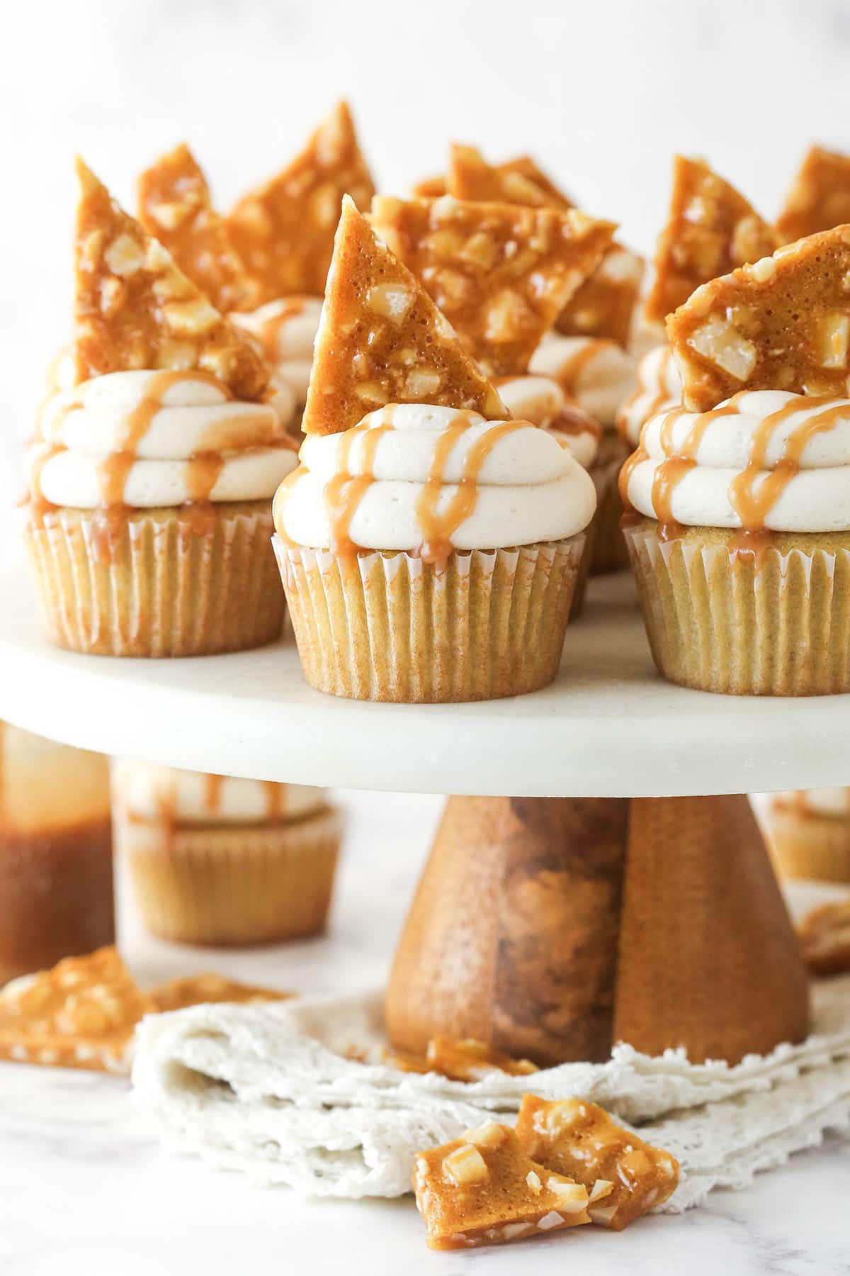 These macadamia brittle cupcakes are moist, sweet, and full of nutty caramel and brown sugar flavor. Topped with homemade brittle. Macadamia Brittle Cupcakes on a cake plate.