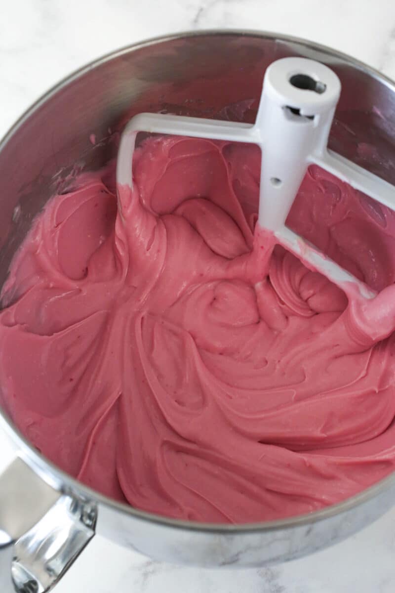 A mixing bowl with cheesecake batter after the strawberry milk, sour cream and extract have been added.