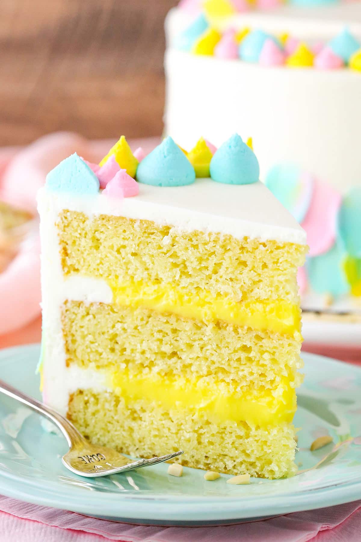 This Almond Custard Layer Cake is made with moist almond cake layers, a smooth almond custard and classic almond frosting! The flavor is light and lovely and I'm a big fan! A slice of Almond Custard Layer Cake next to a fork on a light blue plate