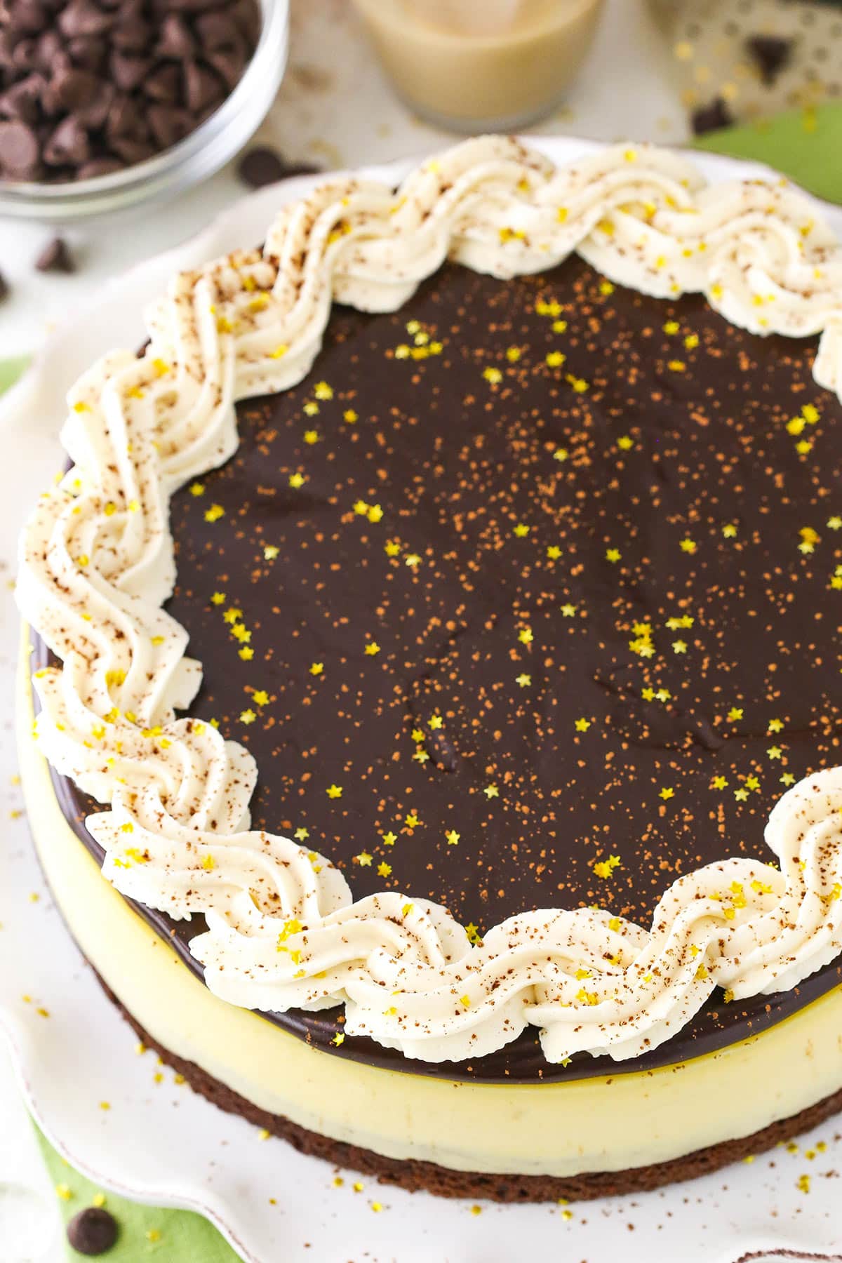 This Baileys Brownie Cheesecake is made with a dense, chewy chocolate brownie on the bottom topped with creamy Baileys cheesecake and finished off with Baileys chocolate ganache and whipped cream! It's all your Baileys dreams come true in one fantastic cheesecake! Overhead view of a full Baileys Brownie Cheesecake on a white platter