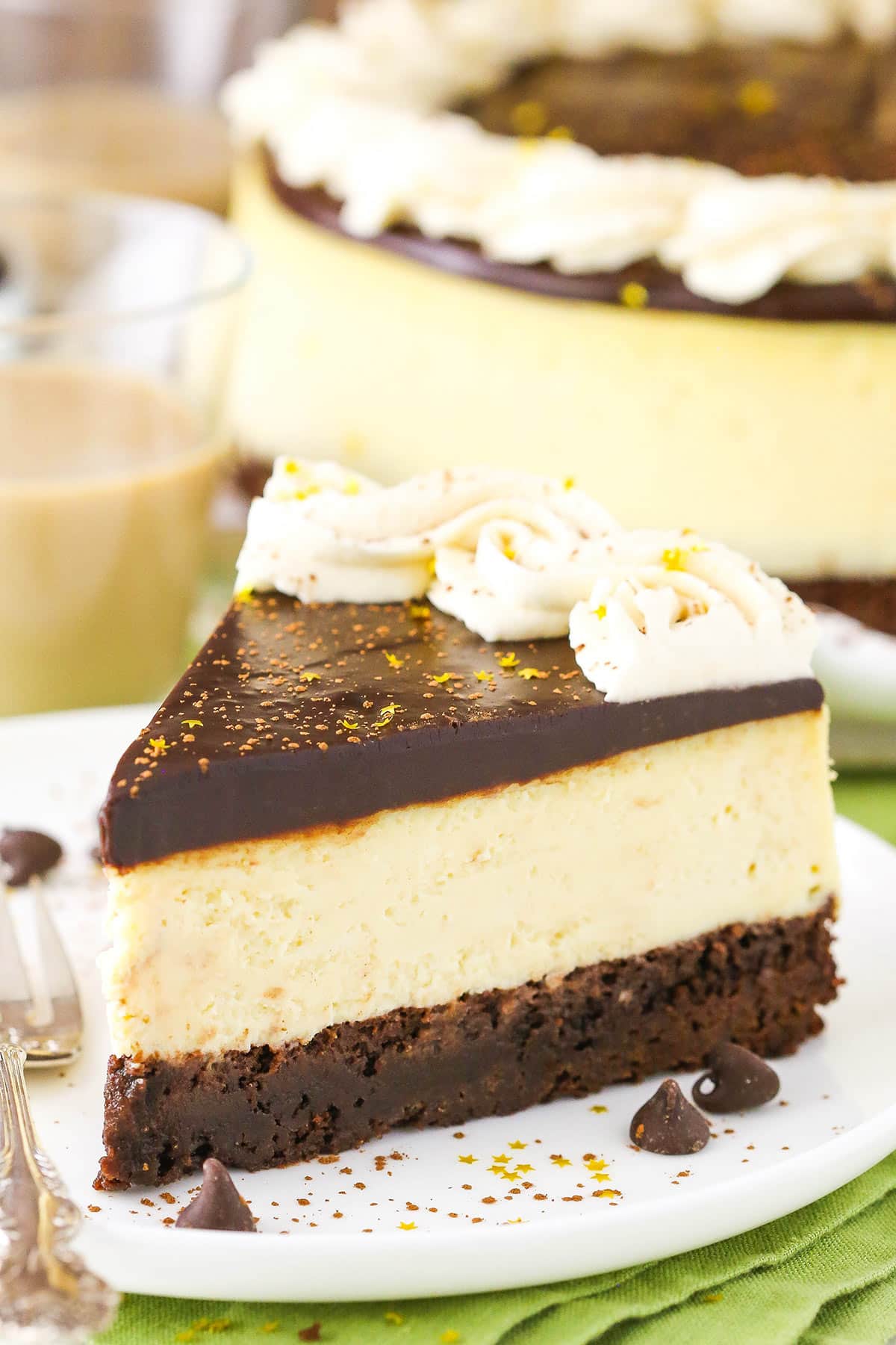 This Baileys Brownie Cheesecake is made with a dense, chewy chocolate brownie on the bottom topped with creamy Baileys cheesecake and finished off with Baileys chocolate ganache and whipped cream! It's all your Baileys dreams come true in one fantastic cheesecake! A slice of Baileys Brownie Cheesecake next to a fork on a white plate