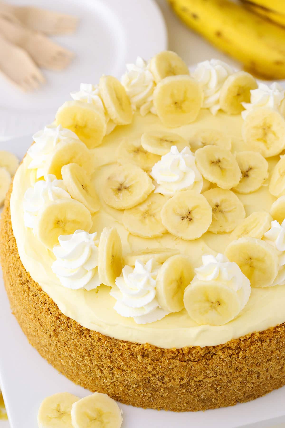 This Banana Cream Cheesecake recipe is made with a fresh banana cheesecake topped with banana bavarian cream! It's smooth, creamy and full of the most amazing banana flavor! Overhead view of a full Banana Cream Cheesecake on a white cake stand