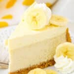 A slice of Banana Cream Cheesecake next to a fork on a white plate