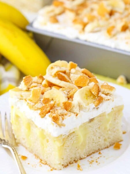 A square serving of Banana Poke Cake next to a fork on a white plate