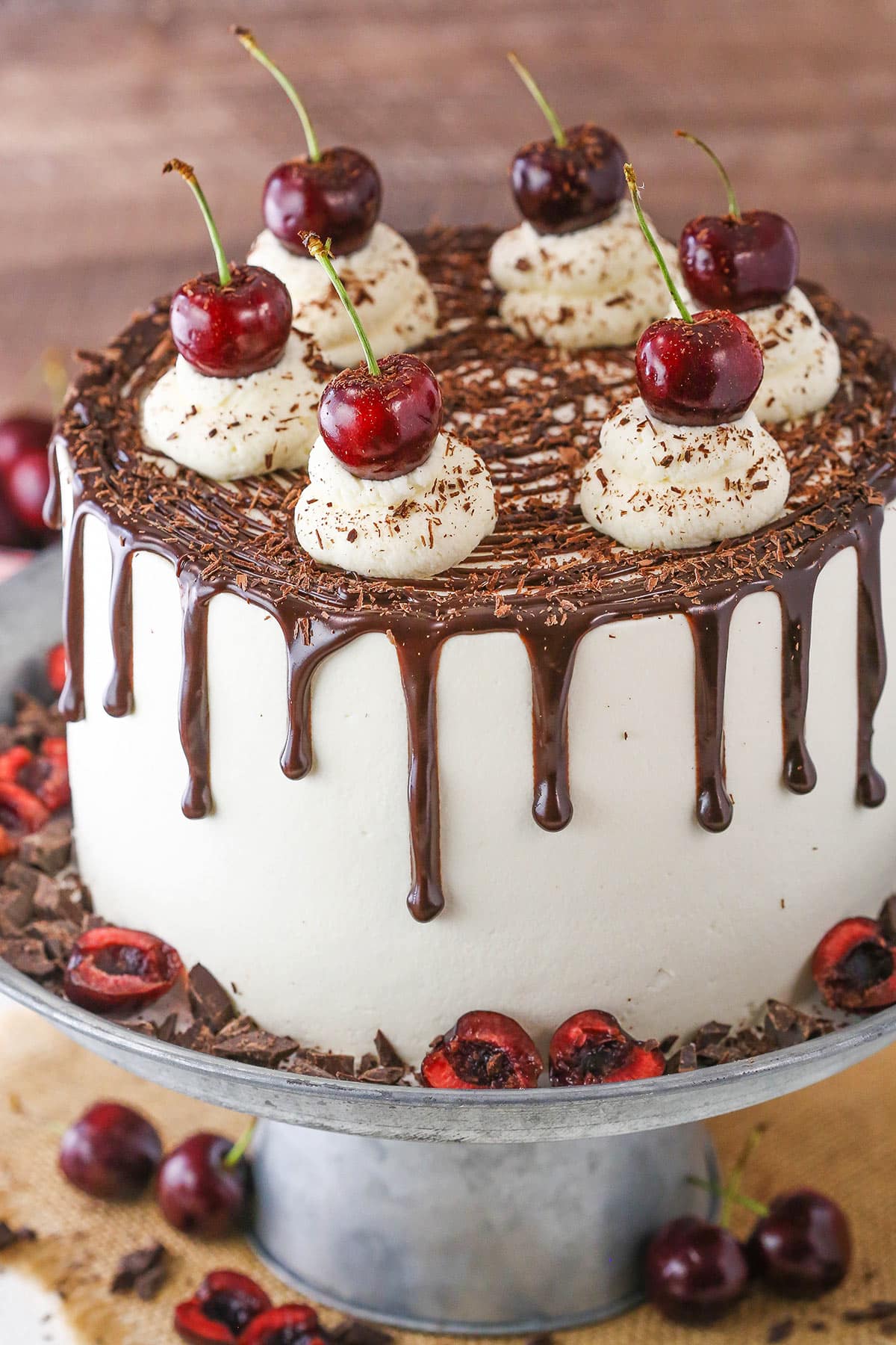 This Black Forest Cake is made with a moist chocolate cake, fresh whipped cream, cherries and cherry liqueur, otherwise known as kirschwasser! It’s moist, delicious and full of flavor! A full Black Forest Cake on a gray cake stand