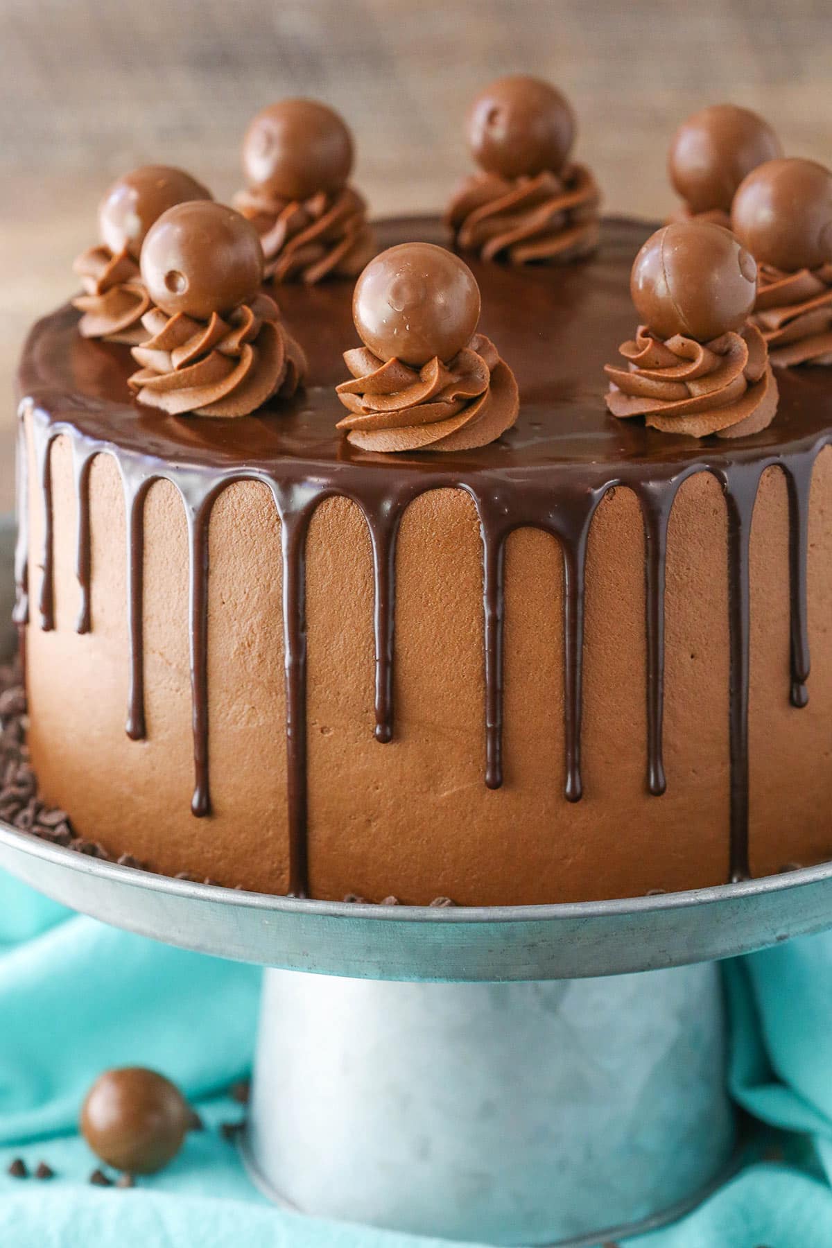 This Drunken Chocolate Truffle Cake is made with a moist chocolate cake recipe, chocolate truffle filling & chocolate frosting - all infused with chocolate liqueur for a delicious "drunken" cake! Side view of a full Drunken Chocolate Truffle Cake on a gray cake stand