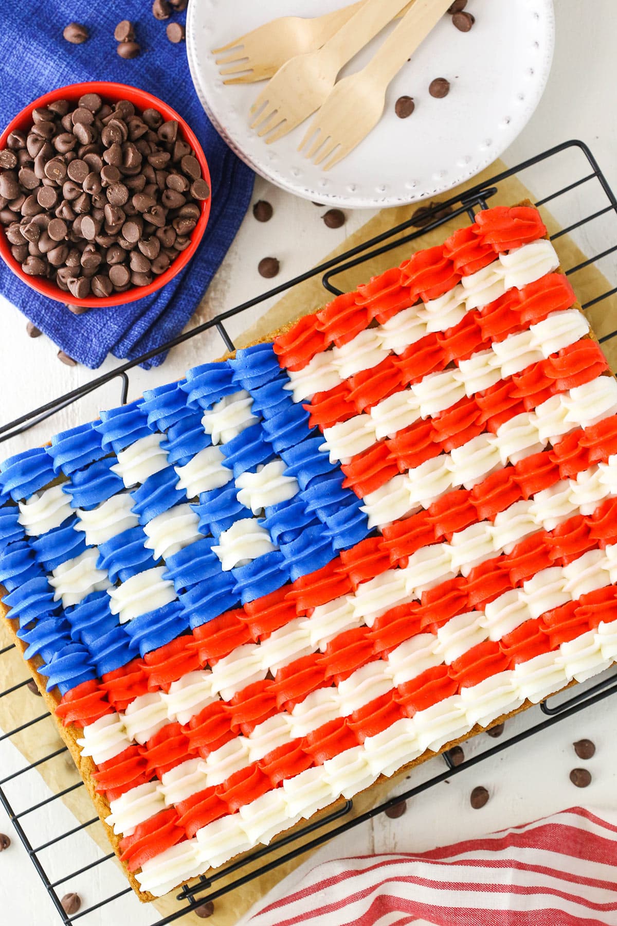 This Flag Chocolate Chip Cookie Cake is a classic 9x13 chocolate chip cookie that's decorated with buttercream in the design of the American flag for the 4th of July! It's delicious, easy to share and the perfect addition to your celebration! Overhead view of a full Flag Chocolate Chip Cookie Cake on a cooling rack