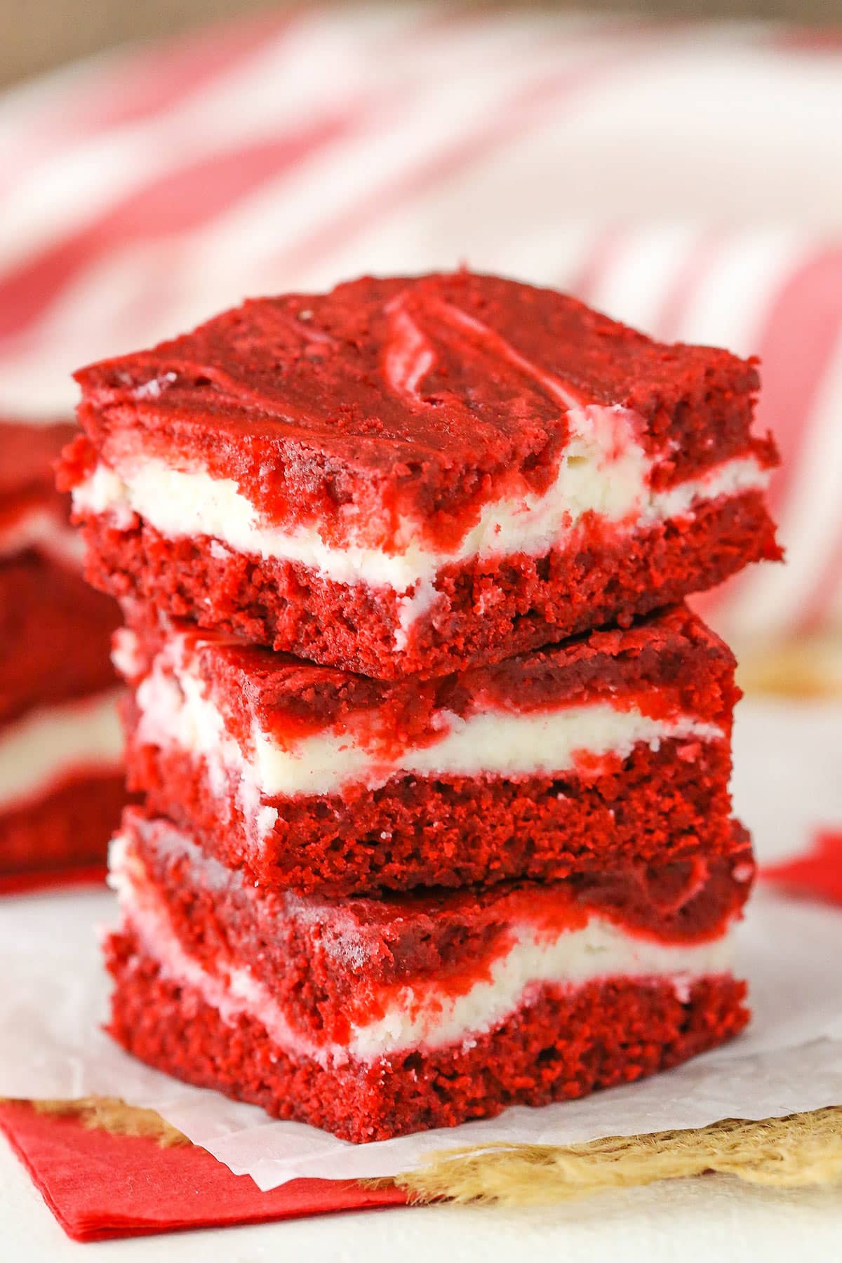 These Red Velvet Cheesecake Swirl Brownies are like the classic cake in bar form! Delicious, sweet and a little tangy! Three Red Velvet Cheesecake Swirl Brownies stacked on a white napkin